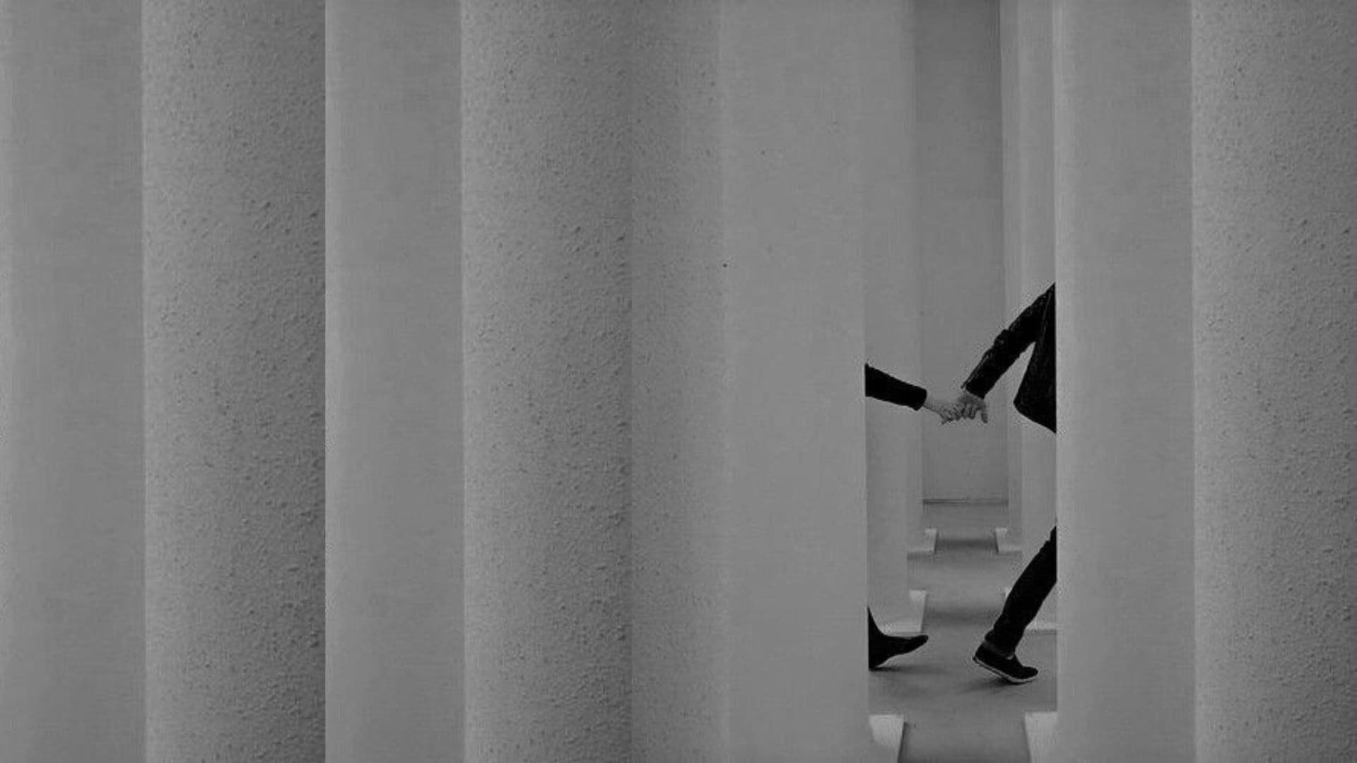 Two people holding hands between architectural concrete columns